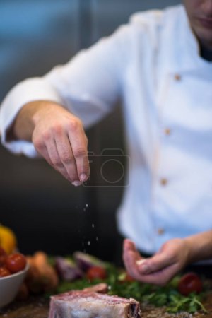 Téléchargez les photos : "Chef mettant du sel sur une tranche juteuse de steak cru
" - en image libre de droit
