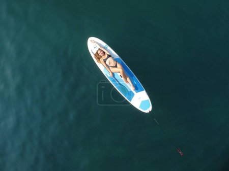 Téléchargez les photos : "Vue aérienne d'un drone sur une jeune femme brune séduisante aux cheveux longs en maillot de bain noir, nageant autour de roches volcaniques, comme en Islande. Vacances d'été et concept de voyage." - en image libre de droit