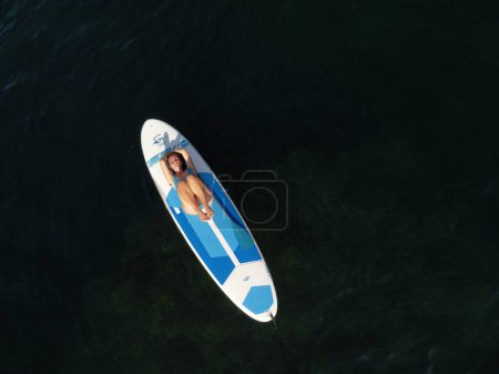Téléchargez les photos : "Vue aérienne d'un drone sur une jeune femme brune séduisante aux cheveux longs en maillot de bain bleu, nageant autour de roches volcaniques, comme en Islande. Vacances d'été et concept de voyage." - en image libre de droit