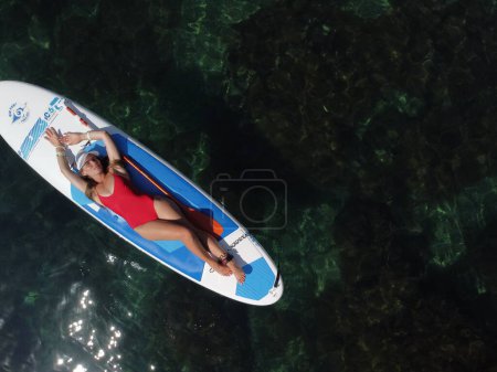 Téléchargez les photos : "Vue aérienne d'un drone sur une jeune femme brune séduisante aux cheveux longs en maillot de bain rouge, nageant autour de roches volcaniques, comme en Islande. Vacances d'été et concept de voyage." - en image libre de droit