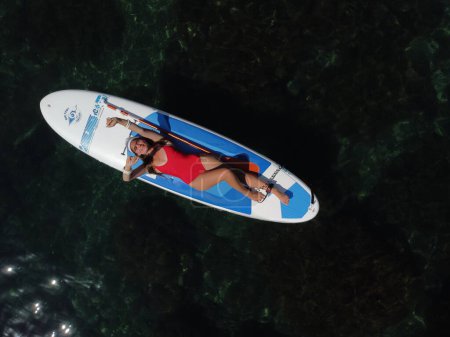 Téléchargez les photos : "Vue aérienne d'un drone sur une jeune femme brune séduisante aux cheveux longs en maillot de bain rouge, nageant autour de roches volcaniques, comme en Islande. Vacances d'été et concept de voyage." - en image libre de droit