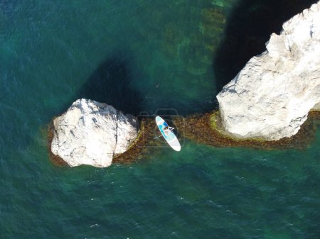 Téléchargez les photos : "Vue aérienne d'un drone sur une jeune femme brune séduisante aux cheveux longs en maillot de bain bleu, nageant autour de roches volcaniques, comme en Islande. Vacances d'été et concept de voyage." - en image libre de droit