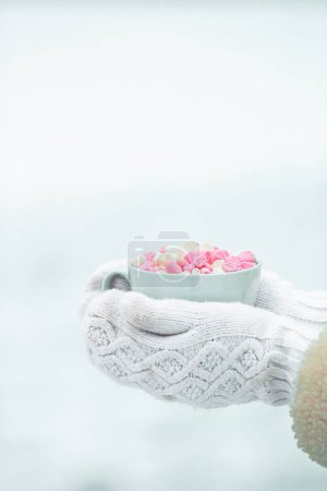 Téléchargez les photos : Les mains féminines tiennent une tasse de café blanc avec des guimauves blanches et roses - en image libre de droit