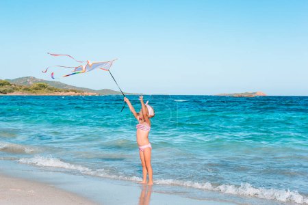 Photo for Little running girl with flying kite on tropical beach. Kid play on ocean shore. - Royalty Free Image