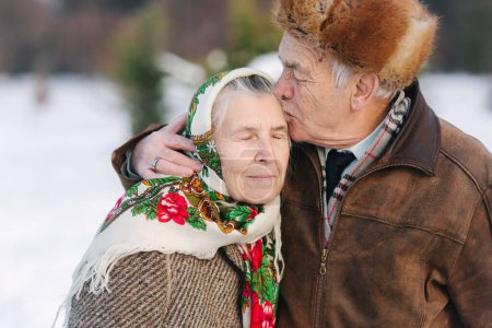 Foto de Retrato de pareja mayor. El anciano besa a su esposa con mucho peso. pareja de ancianos caminando en el parque en invierno. Familia feliz. Boda de oro - Imagen libre de derechos