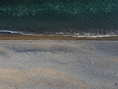 Téléchargez les photos : "Vue aérienne d'en haut sur mer azur et plage de galets. Petites vagues sur une surface d'eau cristalline en mouvement flou. Nature été océan mer plage fond. Personne. Concept vacances, vacances et voyages" - en image libre de droit