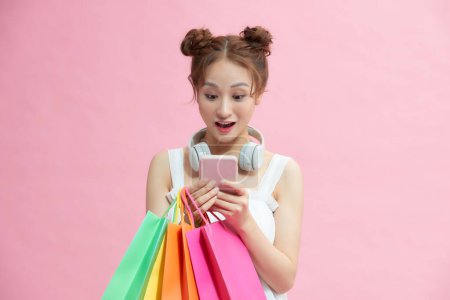 Photo for Young excited cheerful woman holding shopping bags isolated over pink background using mobile phone - Royalty Free Image