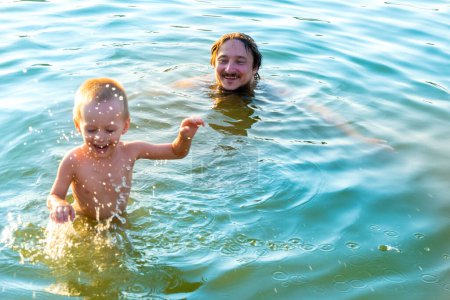 Foto de El niño salpicando con su padre, en las olas del lago. Papá con el niño pequeño de vacaciones. - Imagen libre de derechos