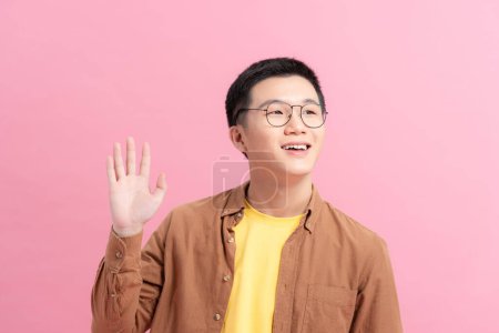 Foto de "Young man wearing casual clothes and glasses waving saying hello happy and smiling, friendly welcome gesture" - Imagen libre de derechos