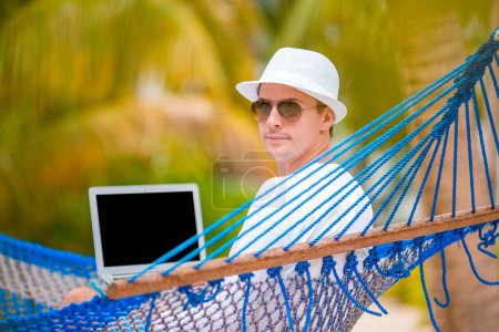 Foto de "Hombre joven con el ordenador portátil en la hamaca en vacaciones tropicales" - Imagen libre de derechos