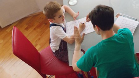 Téléchargez les photos : Mère aidant son petit fils à faire ses devoirs - en image libre de droit