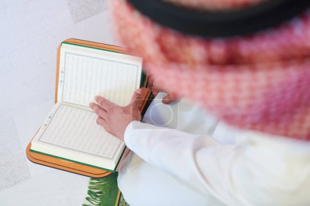 Téléchargez les photos : Arabe musulman lisant le Coran à la maison - en image libre de droit