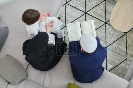 Téléchargez les photos : Vue du dessus de la jeune famille musulmane lisant le Coran pendant le Ramadan - en image libre de droit