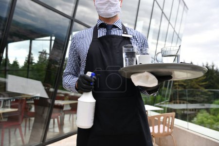 Foto de Camarero limpiando la mesa con spray desinfectante en un restaurante - Imagen libre de derechos