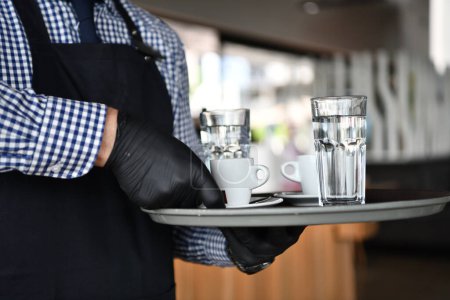 Téléchargez les photos : Serveur dans un masque de protection médicale sert le café au restaurant - en image libre de droit