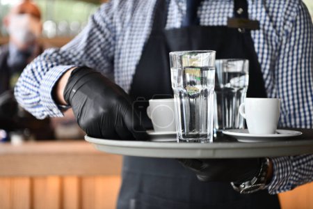 Photo for Waiter in a medical protective mask serves  the coffee in restaurant - Royalty Free Image