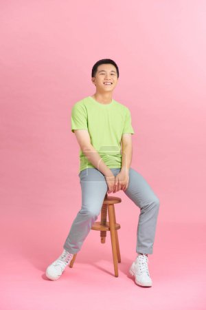 Téléchargez les photos : Homme au t-shirt assis sur une chaise devant un mur rose, look homme - en image libre de droit