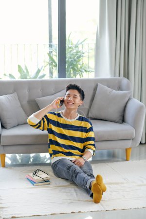 Téléchargez les photos : Jeune homme beau et souriant assis détendu avec un téléphone à la main, - en image libre de droit