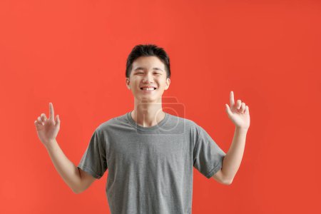 Téléchargez les photos : Happy handsome smiling young Asian man with hands poiting up to empty space above - en image libre de droit