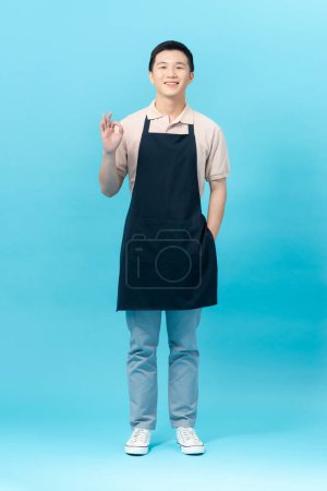 Photo for A full-length shot of a Man wearing an apron saluting with hand with happy expression on isolated background - Royalty Free Image