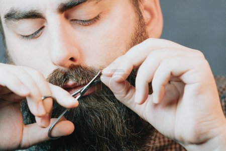 Foto de "Handsome bearded man shaving his beard, Young caucasian bearded man trimming beard in home during quarantine. Lifestyle concept." - Imagen libre de derechos