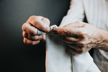 Photo for Seamstress old hands sewing and doing works. Dark background artistic image Cloth working and sewing. Lightful image, copy space, threads of different colors background. Cutting cloth - Royalty Free Image