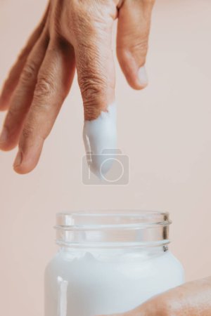 Foto de Elderly woman rubbing hand cream,close-up, minimal, pastel background copy space, self care concept - Imagen libre de derechos