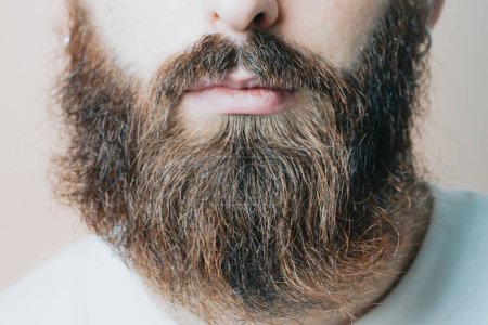 Téléchargez les photos : Beau barbu rasant sa barbe, Jeune homme barbu caucasien taillant la barbe à la maison pendant la quarantaine. Concept de style de vie. - en image libre de droit