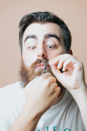 Téléchargez les photos : Jeune homme barbu peigne sa barbe - en image libre de droit