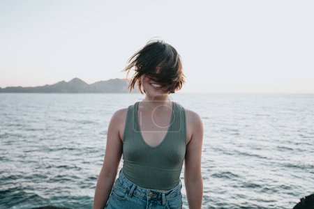 Photo for "A young woman walks on the path of rocks on the shore and looks at the evening sea.Young hipster girl doing some hiking on the shore, traveling and low budget travel concepts, copy space" - Royalty Free Image