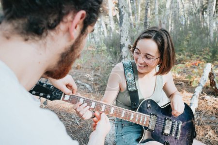 Photo for Handsome Young Man Teaching hipster Girl to Play Guitar at the Park. Concept learning and teaching, forest and nature hobby, free time - Royalty Free Image