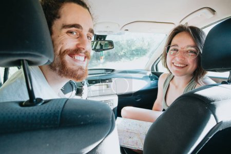 Photo for Young hipster couple using a map on a road trip for directions. Reading a map. Cheerful loving couple relaxing on vacation. Trip on route vacation. Happy and smiling to camera. Decision taking - Royalty Free Image