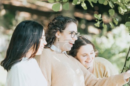 Foto de "Tres mujeres jóvenes divirtiéndose y riendo sin mirar a la cámara durante un día soleado, conceptos de amistad y cuidado" - Imagen libre de derechos