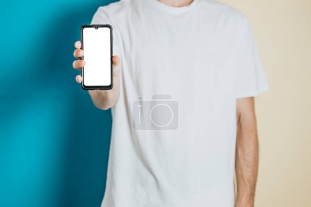 Téléchargez les photos : "Man standing over isolated and holding a phone screen colorful background. Young woman dressed in white t-shirt, blank space t shirt copy space, design, shopping commercial shot" - en image libre de droit