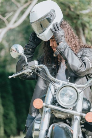 Téléchargez les photos : Portrait d'un jeune homme aux cheveux longs, un vieux motard vêtu d'une veste en cuir sur une moto rétro, moto classique vintage. concept de liberté et de style, un passe-temps pour la vie. espace de copie - en image libre de droit