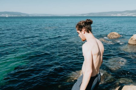 Téléchargez les photos : Jeune homme regardant la mer, avant de sauter dans, vacances méditerranéennes, concepts de liberté et de liberté, moderne, homme pâle - en image libre de droit
