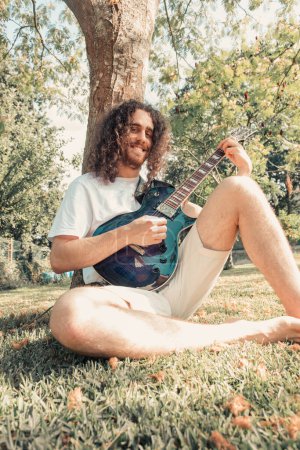 Photo for Attractive man with long hair playing acoustic guitar outdoors, hippie, relax, park lifestyle, hobby, copy space - Royalty Free Image