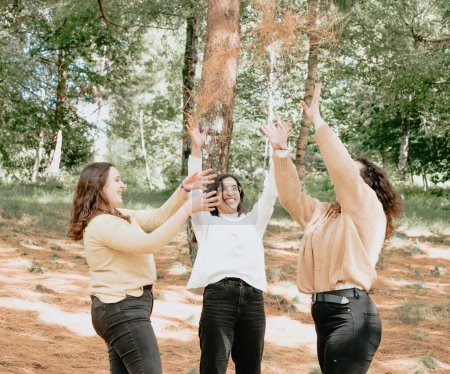 Téléchargez les photos : "3 young woman having fun playing together in the forest, young students celebrating graduation and notes" - en image libre de droit