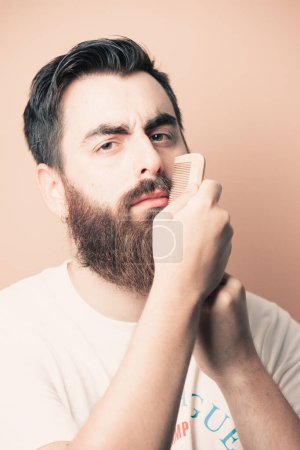 Téléchargez les photos : Handsome bearded man shaving his beard, Young caucasian bearded man trimming beard in home during quarantine. Lifestyle concept. - en image libre de droit