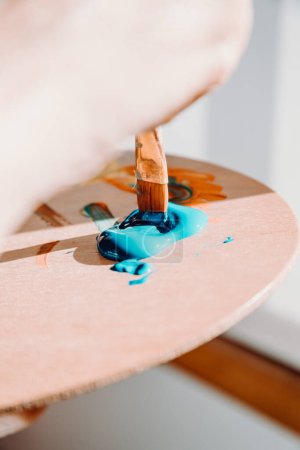 Foto de Close up of paintbrush picking blue color from an artist palette. Colorful image from an artists studio or a school showing creative education - Imagen libre de derechos