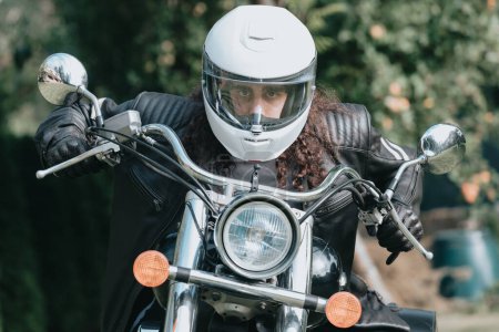 Foto de Portrait of a young long hair man, an old biker in a leather jacket on a retro bike, vintage classic motorcycle. concept of freedom and style, a hobby for life. copy space - Imagen libre de derechos