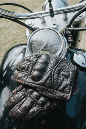 Foto de Close up of a pair of gloves over motorbike. Travel concept. Gloves and rude hands holding a map overa old school motorbike. Copy space. Quitting gloves - Imagen libre de derechos