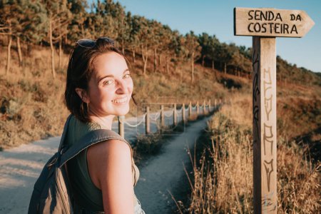 Photo for Young hipster girl turning around smiling to camera while doing some hiking on the shore, traveling and low budget travel concepts, copy space - Royalty Free Image
