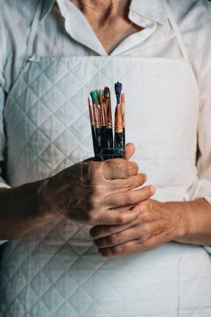 Téléchargez les photos : Woman artist painter holding a bunch of paint brush. Painter artist and paintbrush in studio, Crystal bottle, indie style, hipster, creative concept - en image libre de droit
