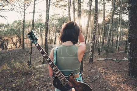Photo for "Back shot of a young woman holding a guitar during a sunset, enjoy music life concept." - Royalty Free Image