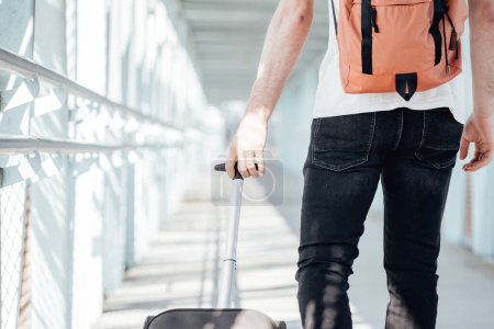 Photo for Back shot of a traveler carrying his luggage and bags at the airport or bus station during a travel. Hipster modern traveler, sunny day, copy space. - Royalty Free Image