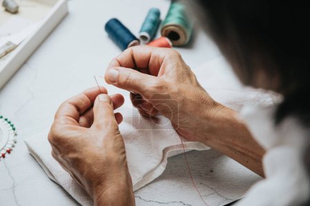 Photo for Close up on woman's hands sewing needle and thread. Old woman working wasted hands .Tailor sewing some fabric. Details, low light, moody - Royalty Free Image