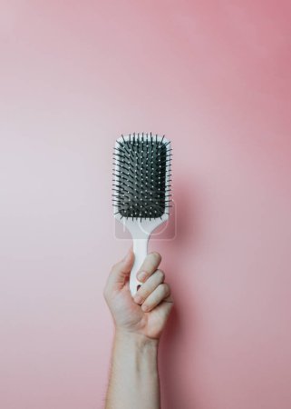 Photo for Minimal image of a hand holding an hair comb over a light color background, copy space, minimal image. Hair styling concept, beauty styling - Royalty Free Image