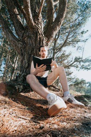 Photo for Young hippie male reading a book, wide angle shot, social network, summer vibes relaxed lifestyle - Royalty Free Image