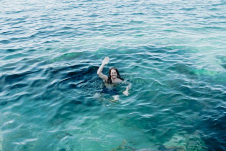 Foto de Joven flotando en el océano durante sus vacaciones en España, mar cristalino, saludando a la cámara, espacio para copiar - Imagen libre de derechos